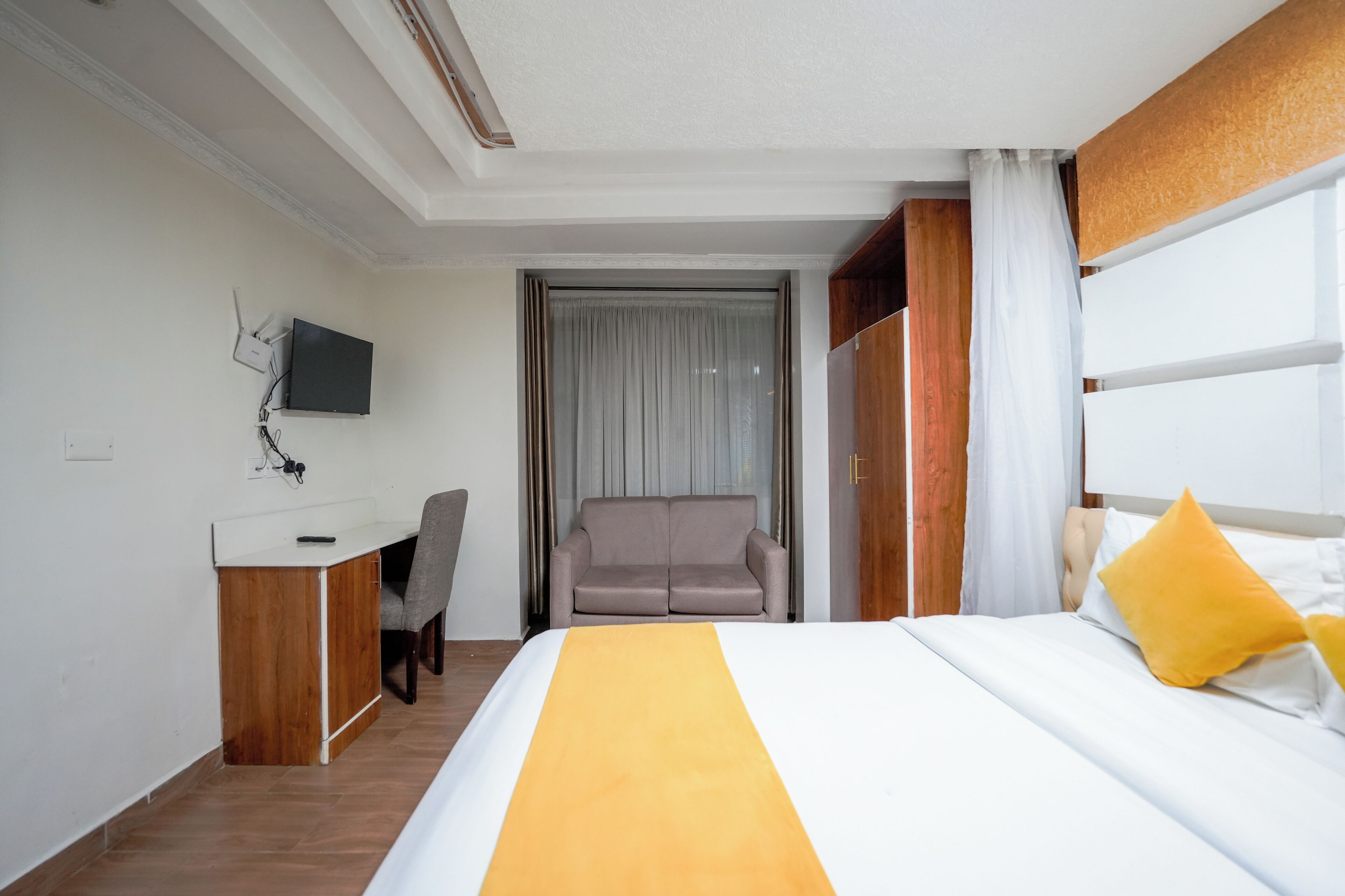 Una camera d'albergo con un letto, una scrivania con una sedia, una televisione e una finestra con tende.