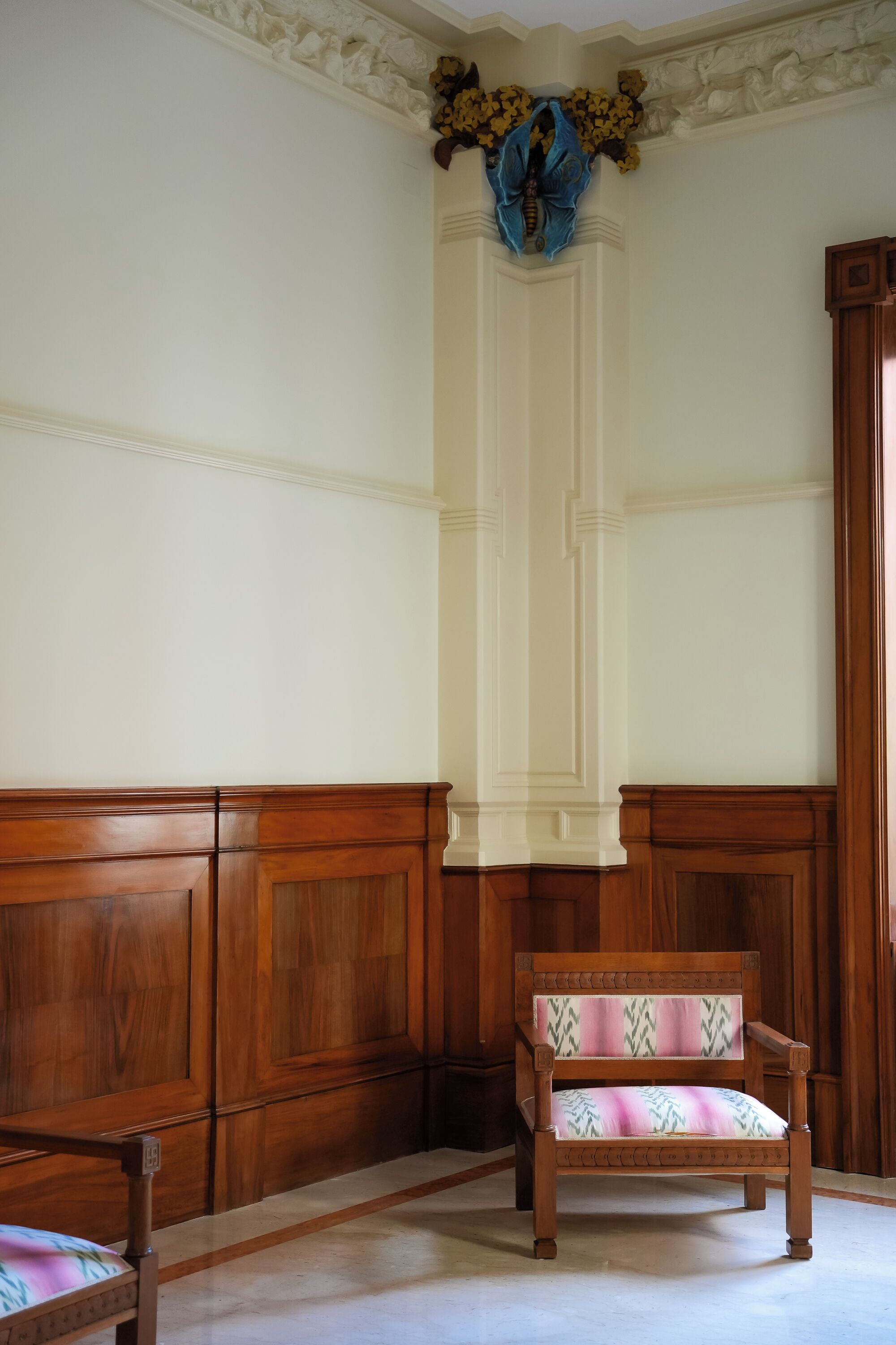 Um quarto com um banco de madeira, parede branca com moldura decorativa e uma porta de madeira.
