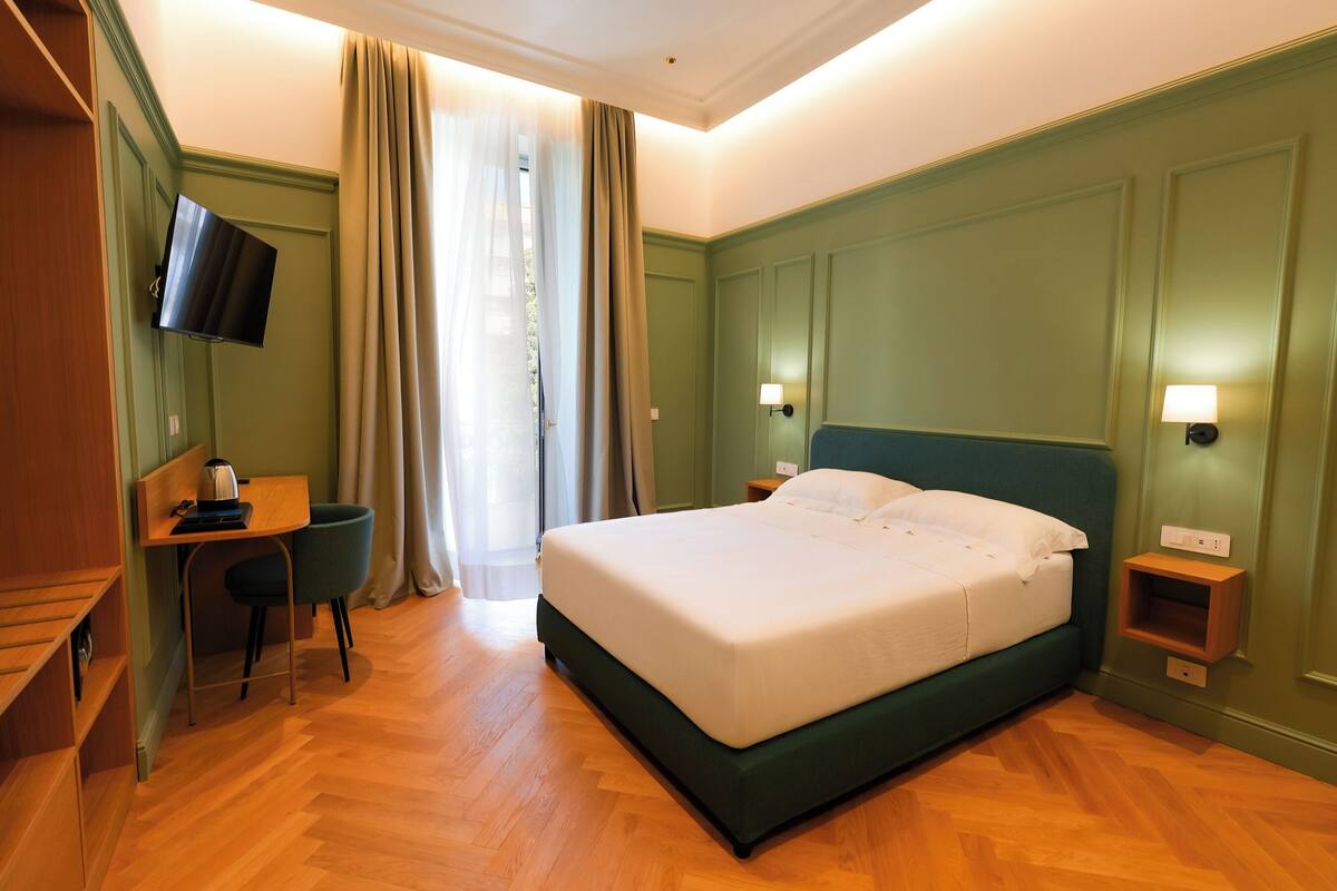 Une chambre d’hôtel avec un grand lit, un bureau, une chaise, une télévision et une fenêtre avec des rideaux.