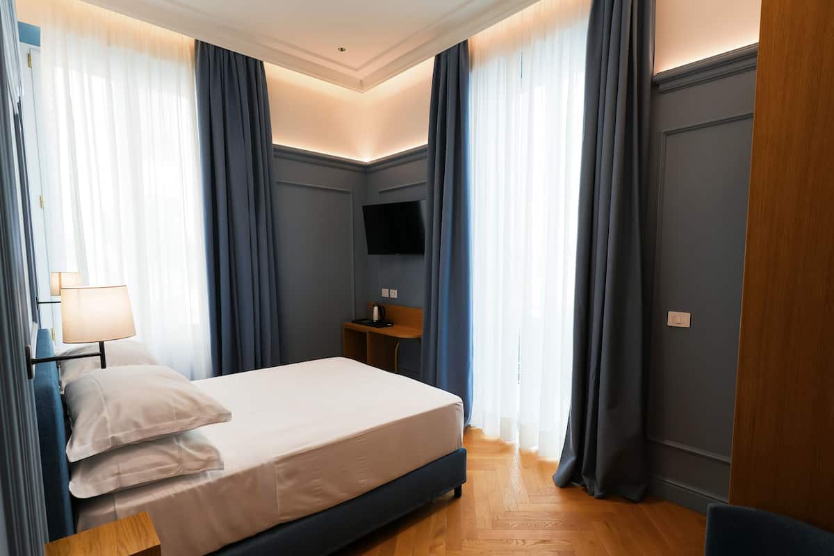 Une chambre d’hôtel avec un lit, une table de chevet avec une lampe, un téléviseur fixé au mur et un plancher en bois.