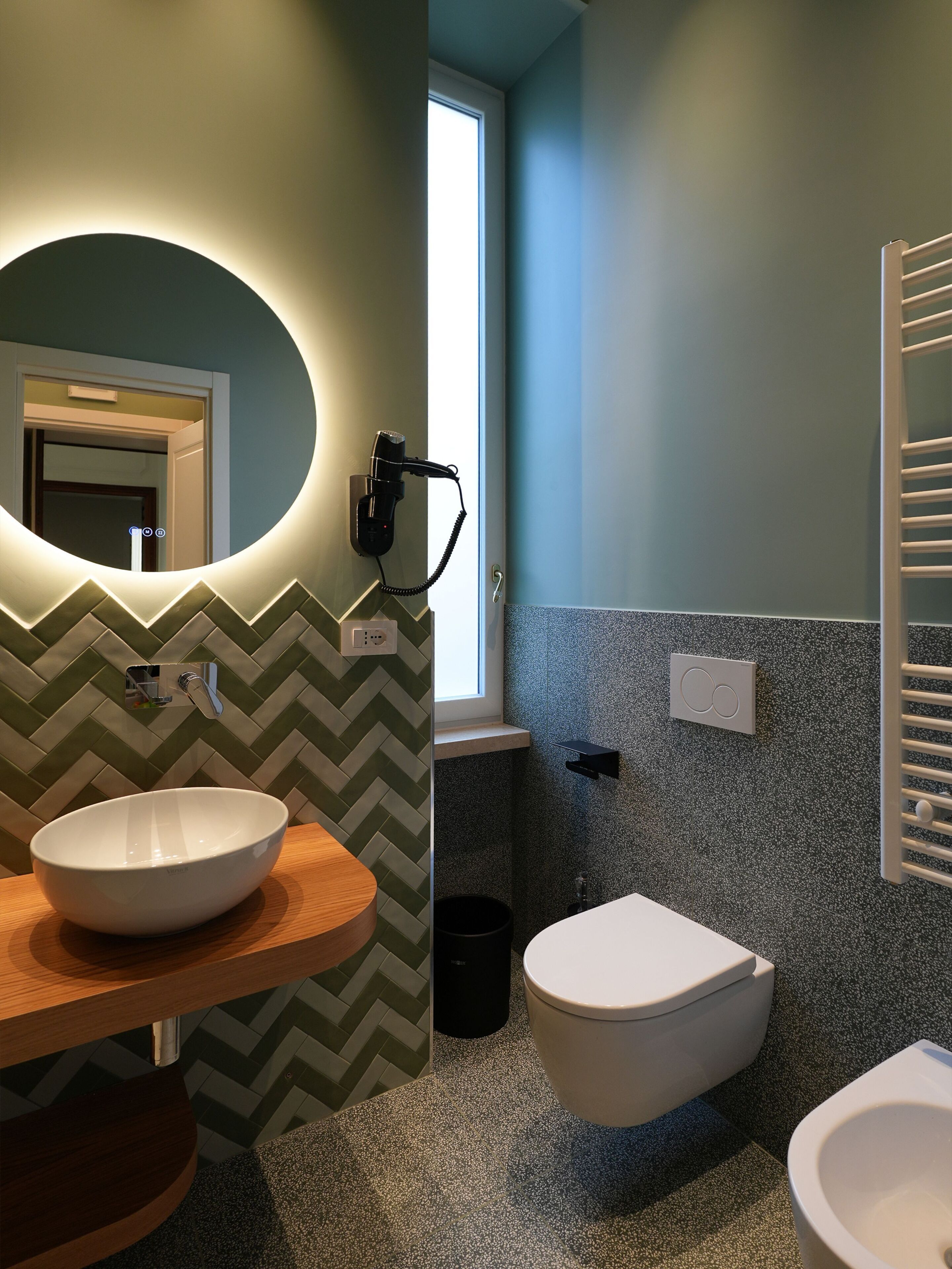 Une salle de bain moderne avec un grand miroir, un lavabo sur colonne, des toilettes et un porte-serviettes.