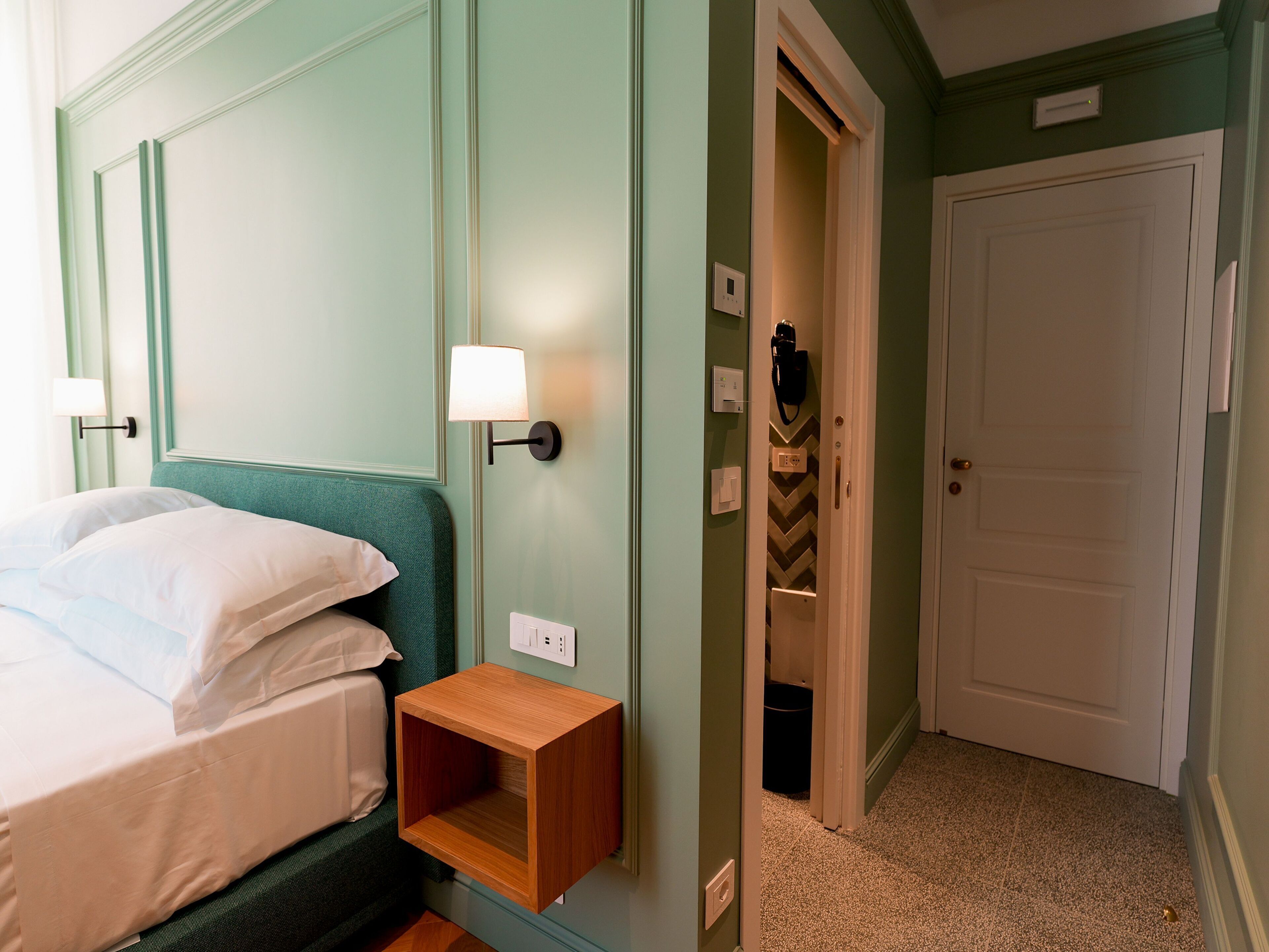 Una habitación de hotel con cama, lámpara de noche y una mesita de noche de madera.