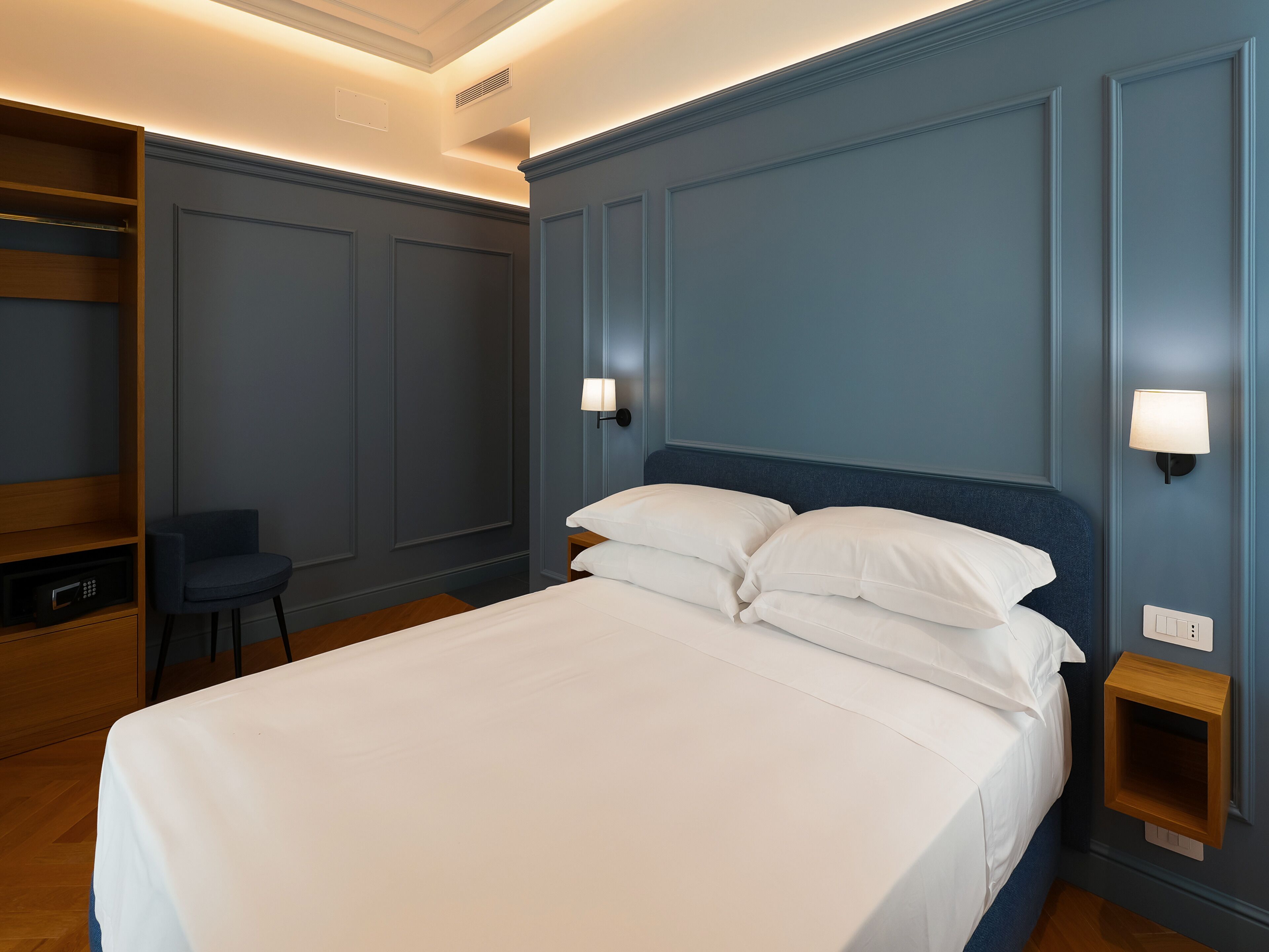 Een verzorgd hotelkamer met een bed, nachtkastjes, een stoel en inbouwkasten.