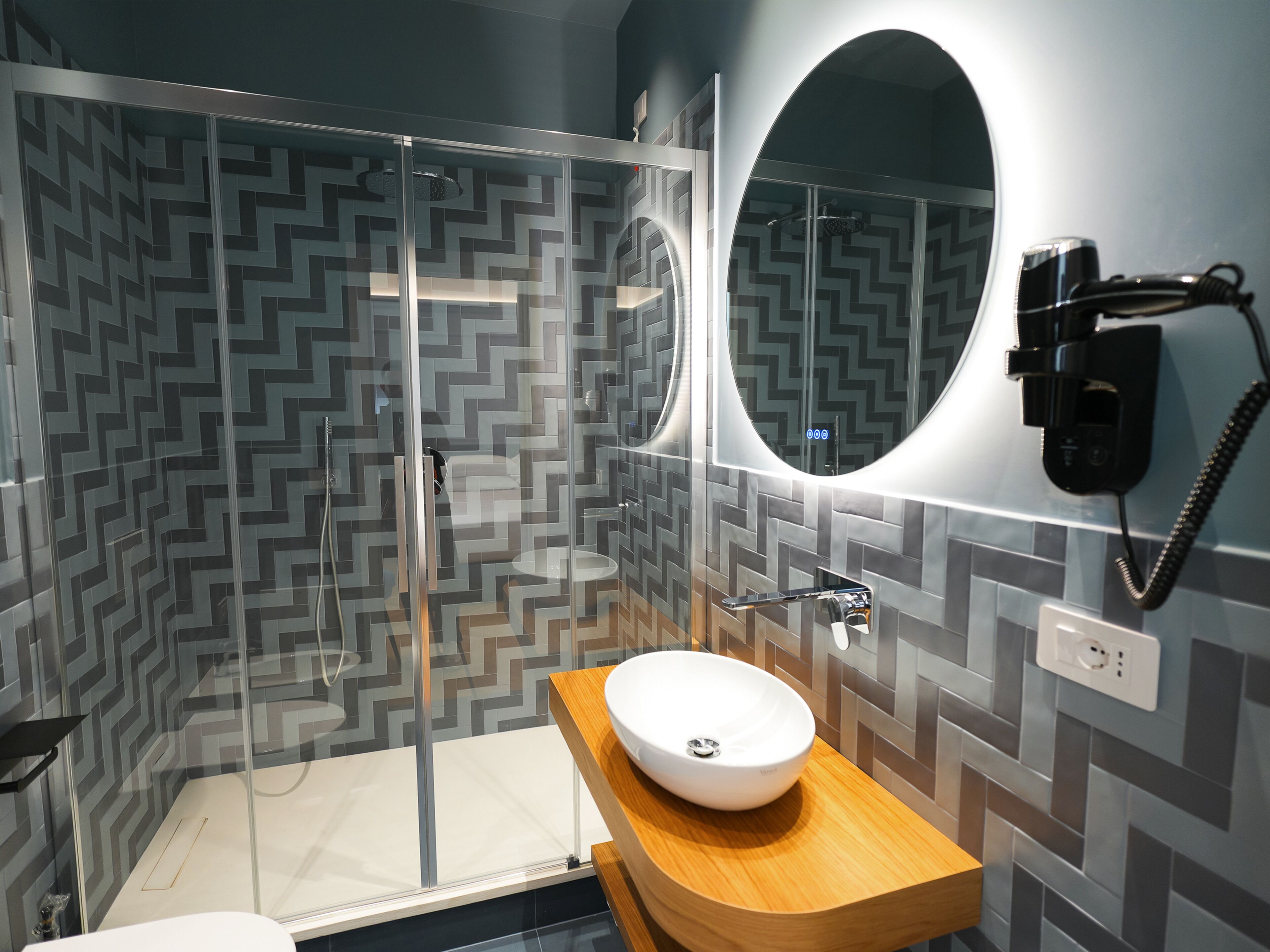 Een moderne badkamer met een douchecabine van glas, een houten wastafelmeubel en een ronde spiegel.