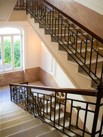 Una gran escalera con barandales negros decorados y detalles dorados, que conduce a un piso superior.