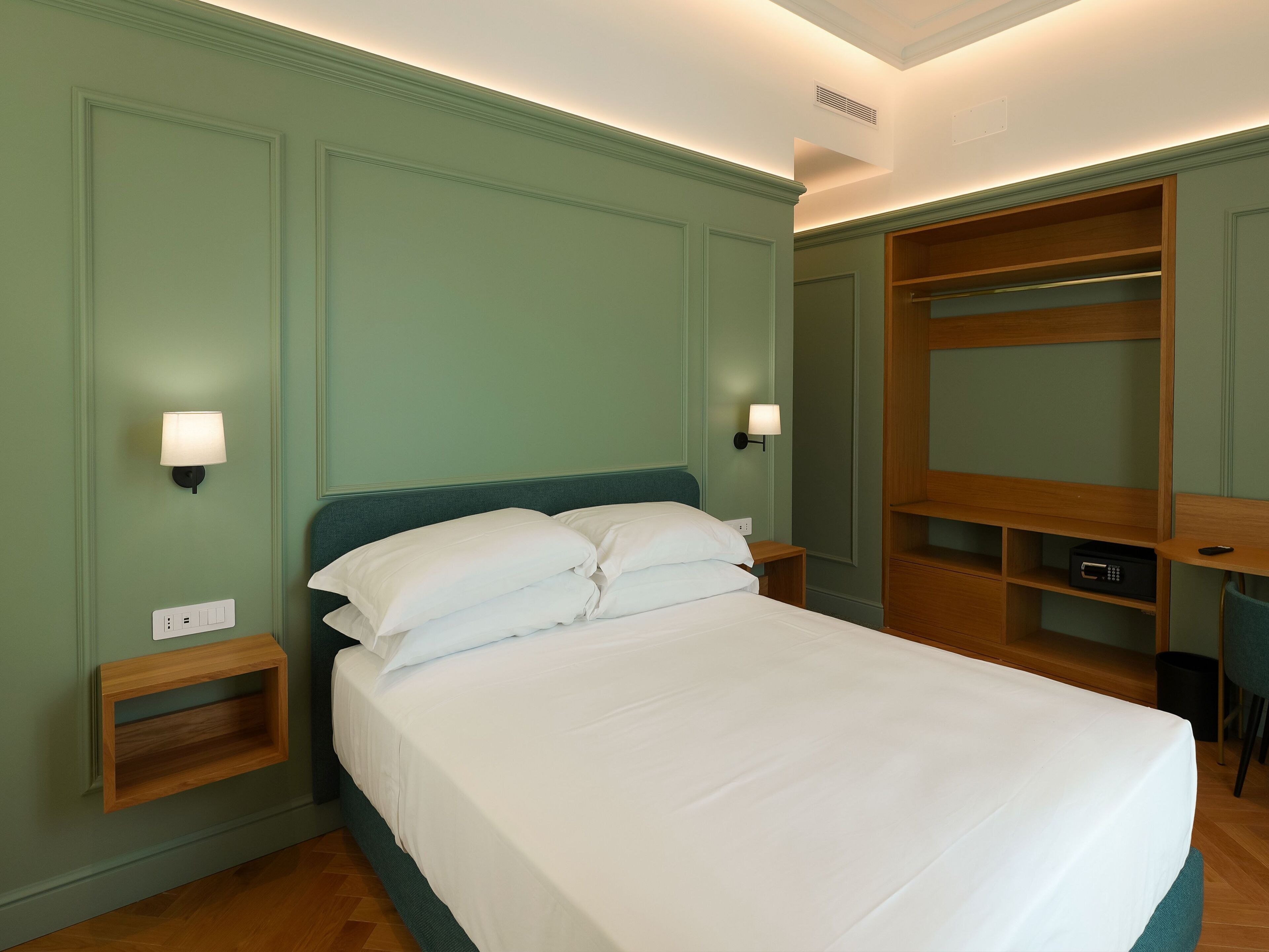 A neatly made bed with white linens in a room with green walls and wooden furniture.