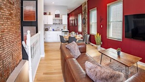 A modern living room with a brown leather sofa, a wooden coffee table, and a red accent wall. - Stylish 2BR/2BA House in The Grove w/ Free Parking (St. Louis)