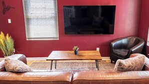 A living room with a red wall, a wooden coffee table, a leather sofa, a black leather armchair, and a flat-screen TV mounted on the wall. - Stylish 2BR/2BA House in The Grove w/ Free Parking (St. Louis)