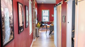A hallway with red walls, wooden flooring, and a dining area with a table and chairs. - Stylish 2BR/2BA House in The Grove w/ Free Parking (St. Louis)