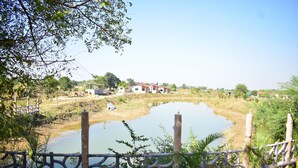A rustic wooden fence surrounding a pond with a small house in the background. - Ajinkya Jungle lake farms resort (Chimur)