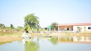 A calm river with boats and a building with a red roof in the background. - Ajinkya Jungle lake farms resort (Chimur)
