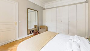A hotel room with a large bed, a wardrobe, a mirror, and a seating area. - Elegant apartment with suite - Arc de triomphe (Paris)