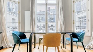 A room with a table and two chairs, a window with curtains, and a view of buildings outside. - Elegant apartment with suite - Arc de triomphe (Paris)