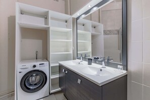 Une salle de bain moderne dotée d’un lave-linge intégré, d’un grand miroir et d’un meuble-lavabo à deux vasques.