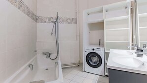 A bathroom with a bathtub, a shower, a washing machine, and a sink. - Elegant apartment with suite - Arc de triomphe (Paris)