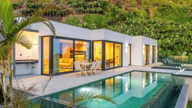 Ein modernes Haus mit Schwimmbad, Glasüren und einem Essbereich.