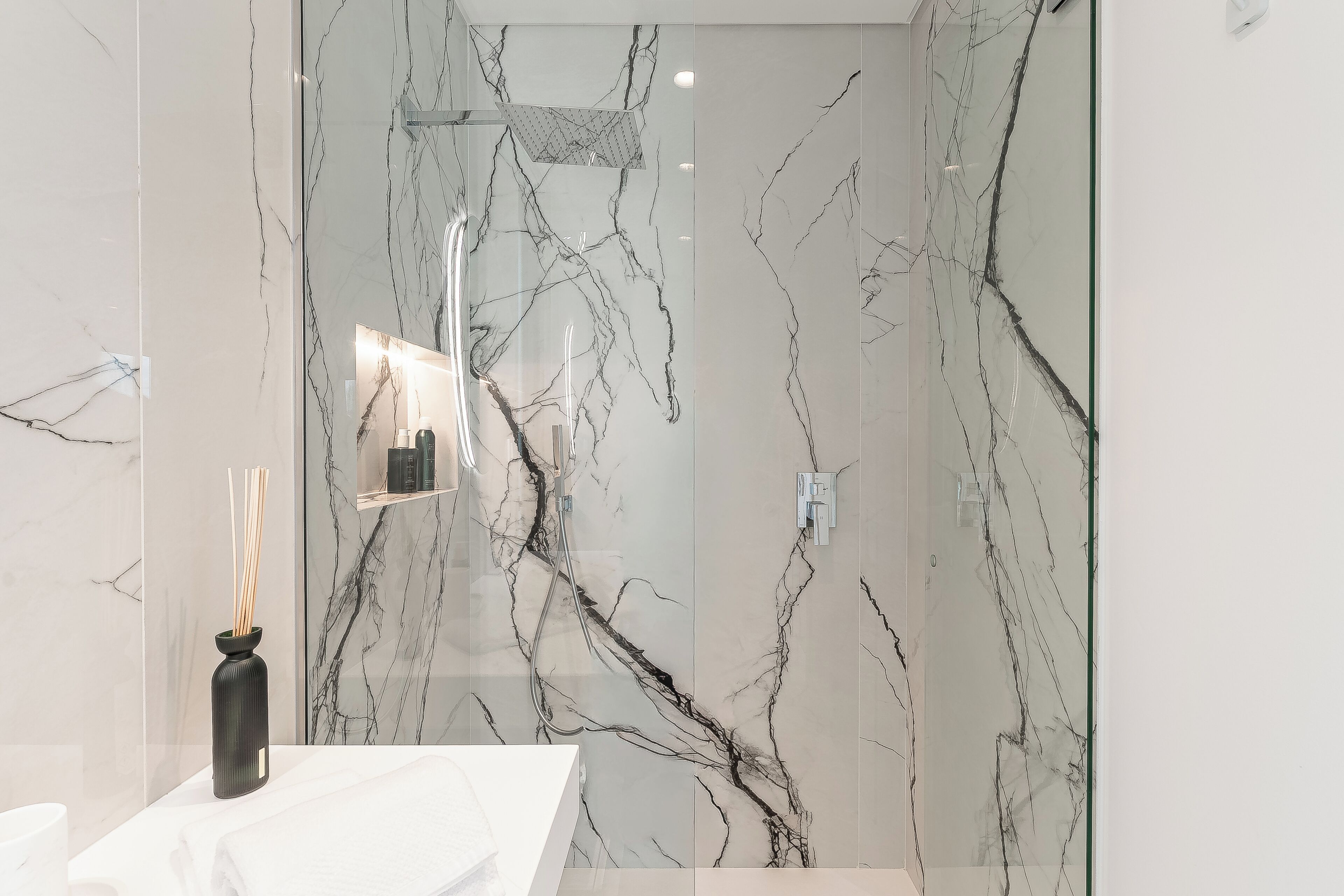 A bathroom with a marble wall, a glass shower enclosure, and a white sink.