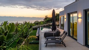 Eine moderne Außenpatio mit Pool, Liegestühlen und Blick auf das Meer.
