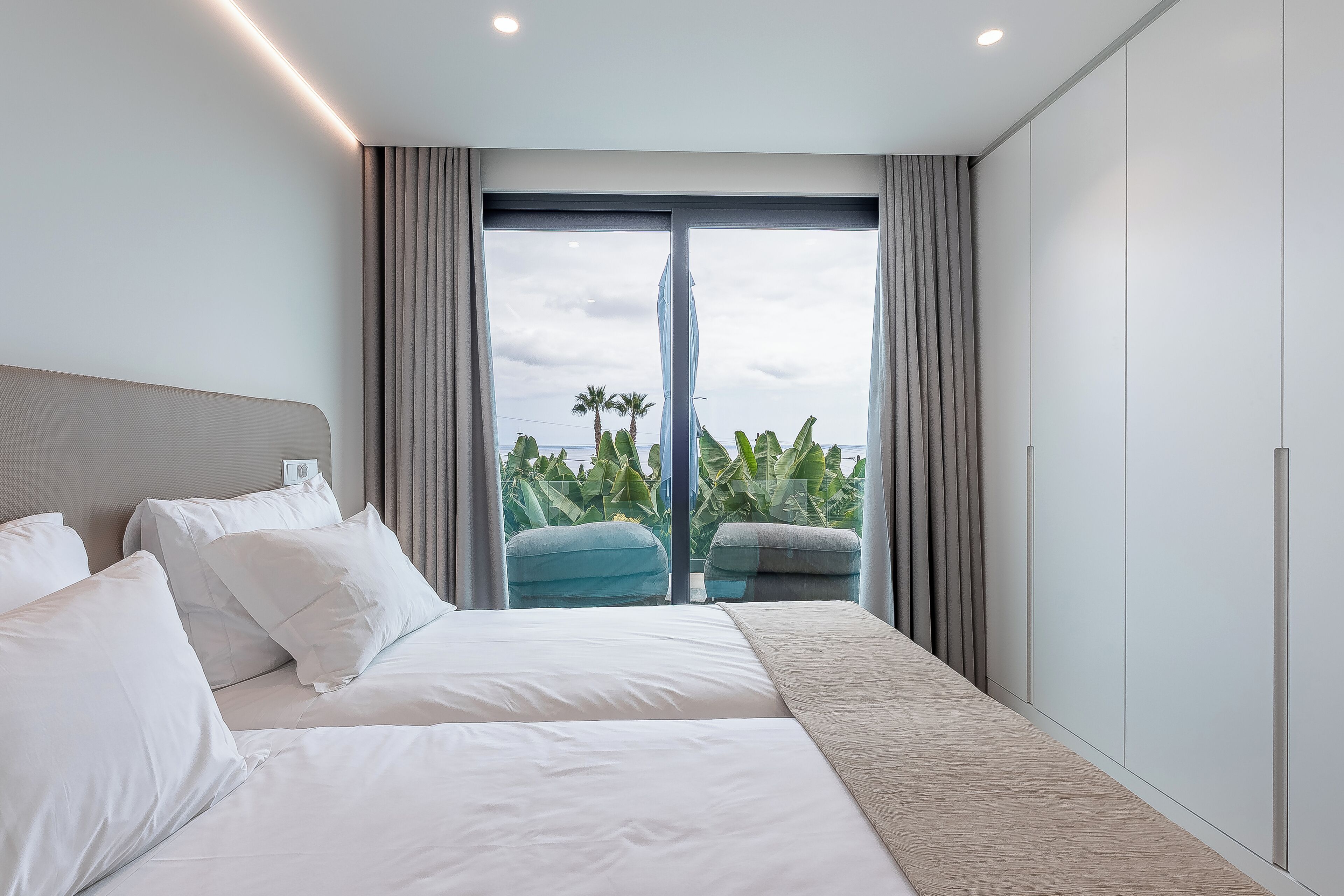 Une chambre d’hôtel moderne avec un grand lit, une vue sur les palmiers et un balcon agrémenté de rideaux.