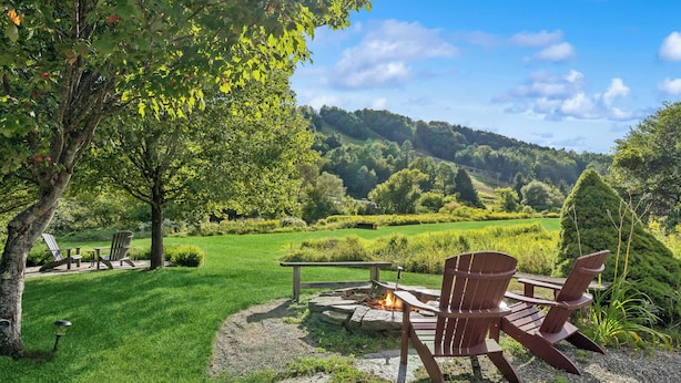 A garden with a fire pit, Adirondack chairs, and a view of a green landscape. - Saskadena Lodge & Little House, Full Property (Pomfret)