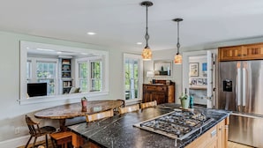A kitchen with a large island, built-in shelves, a refrigerator, and pendant lighting. - Saskadena Lodge & Little House, Full Property (Pomfret)