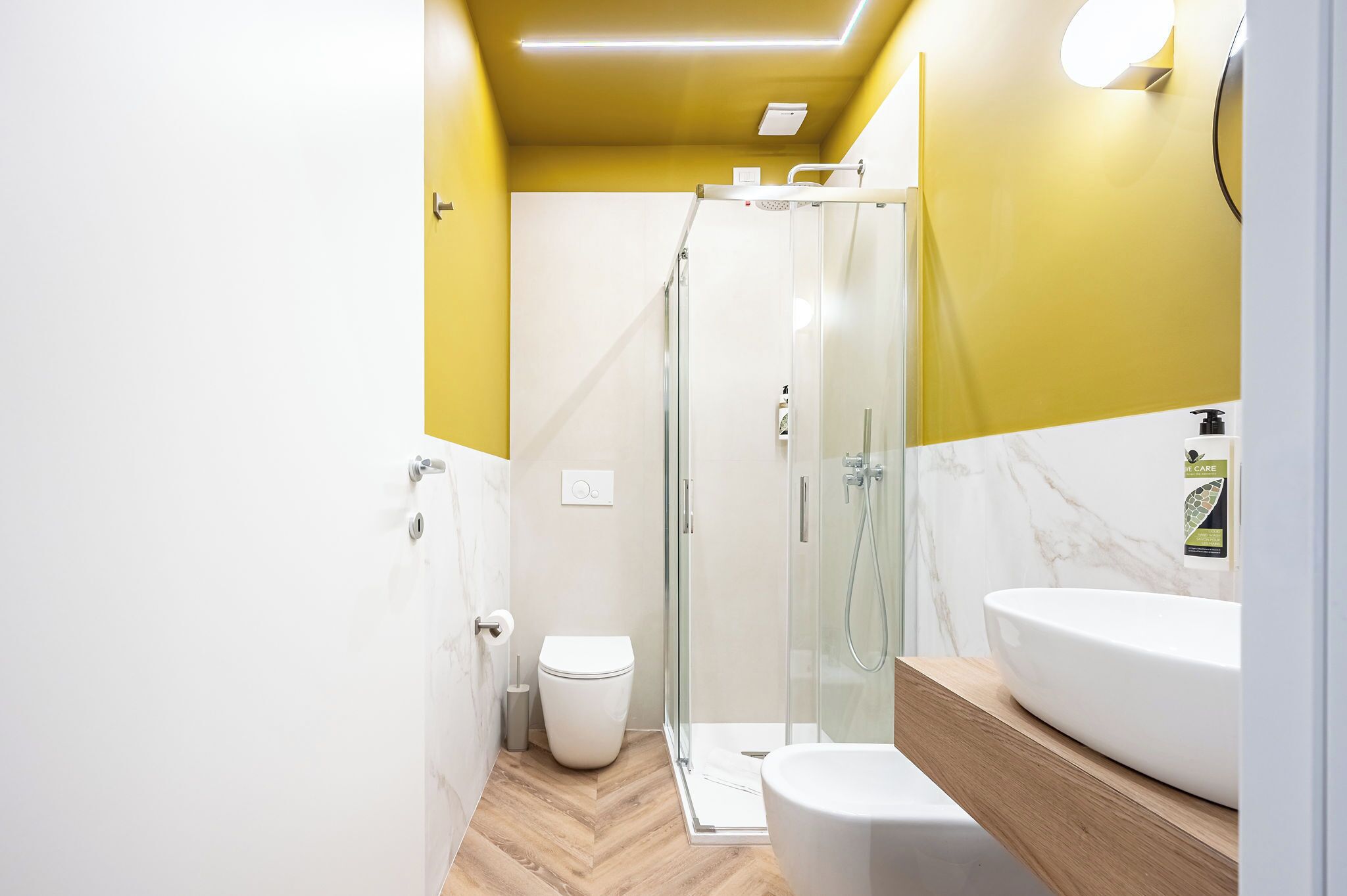 Ein modernes Badezimmer mit einer gläsernen Dusche, einer weißen Toilette und einem weißen Waschbecken mit Holzbeschlag.