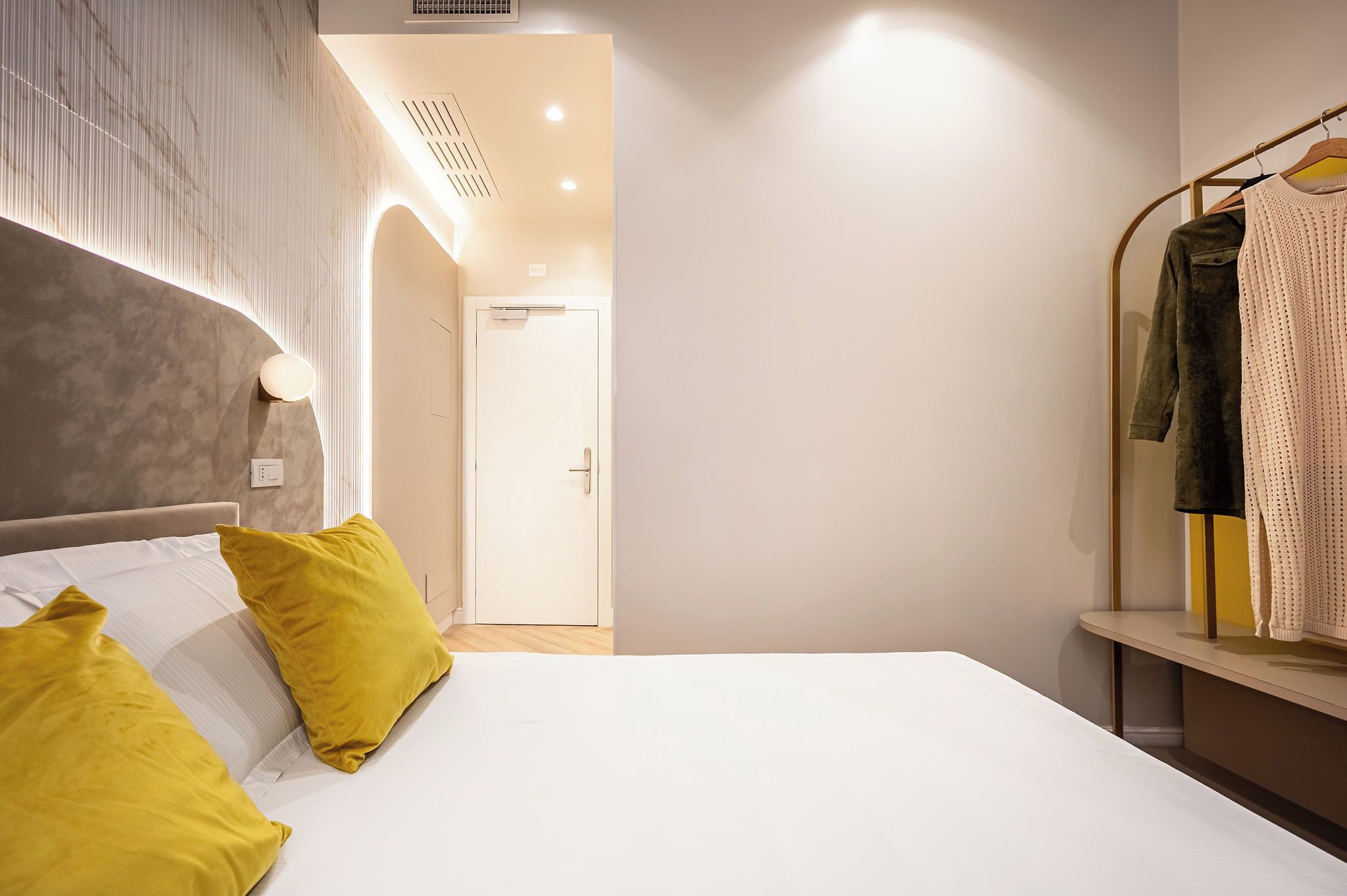 A modern hotel room with a bed, a wardrobe, and a door leading to another room.