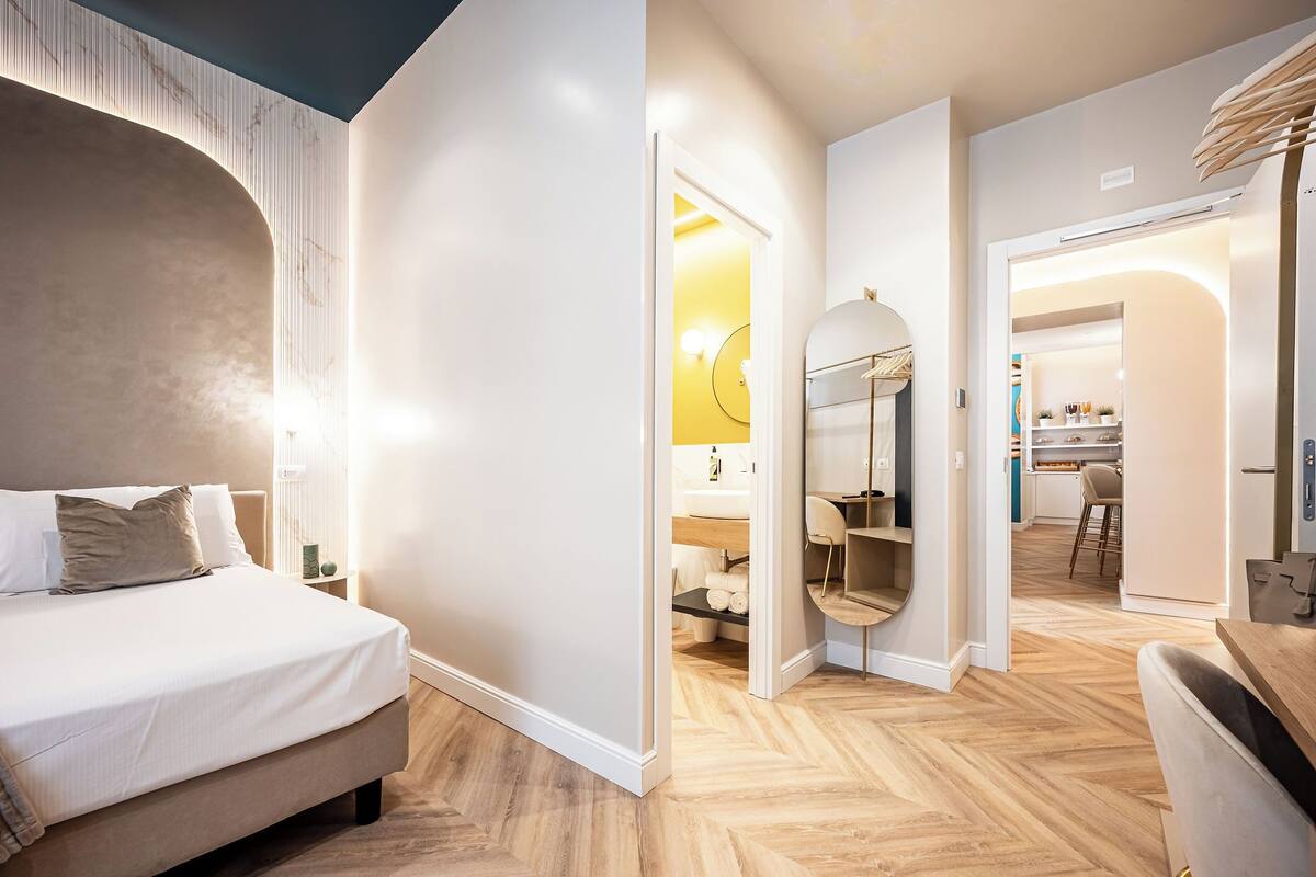 Una habitación de hotel moderna con una cama grande, un baño con espejo y una zona de comedor con mesa y sillas.