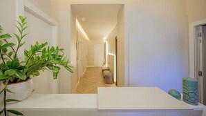 Un couloir doté d’un parquet en bois disposé en motif «point de Hongrie», une plante en pot, une petite table sur laquelle repose un objet décoratif vert, et une porte au fond.