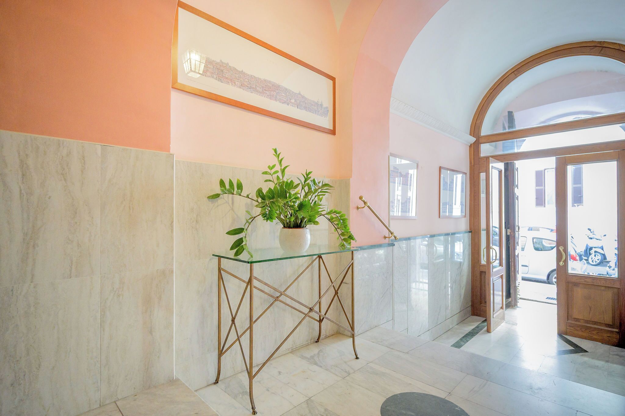 A reception area with a marble floor, a glass-top console table with a potted plant, and a framed picture on the wall.