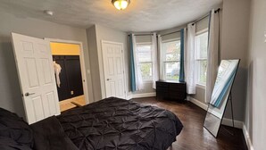 Quarto com cama, cômoda, armário e uma janela grande com cortinas.