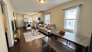 Uma sala de estar moderna com sofá, mesa de centro e mesa de jantar. Há uma cozinha com armários e eletrodomésticos.