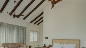 A spacious bedroom with a large bed, a wooden ceiling fan, a sofa, and a coffee table. - Amã Stays & Trails Mudita Estates, Goa (Morjim)