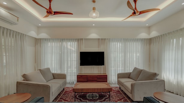 A modern living room with two sofas, a coffee table, a TV, and ceiling fans. - Amã Stays & Trails Mudita Estates, Goa (Morjim)