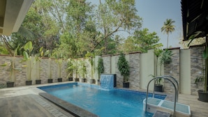 A rectangular swimming pool with a tiled edge, surrounded by a stone wall and potted plants. - Amã Stays & Trails Mudita Estates, Goa (Morjim)