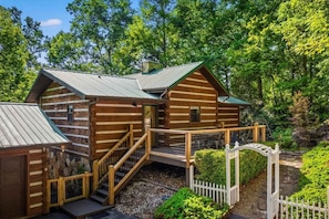 A log cabin with a porch, a staircase, and a white picket fence.
