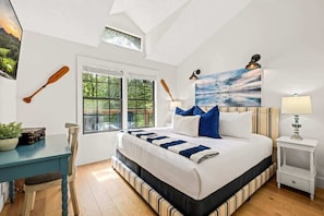 A bedroom with a bed, a window, a desk, a chair, and a lamp.