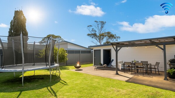 A backyard with a trampoline, a fire pit, and a covered patio area with outdoor furniture.