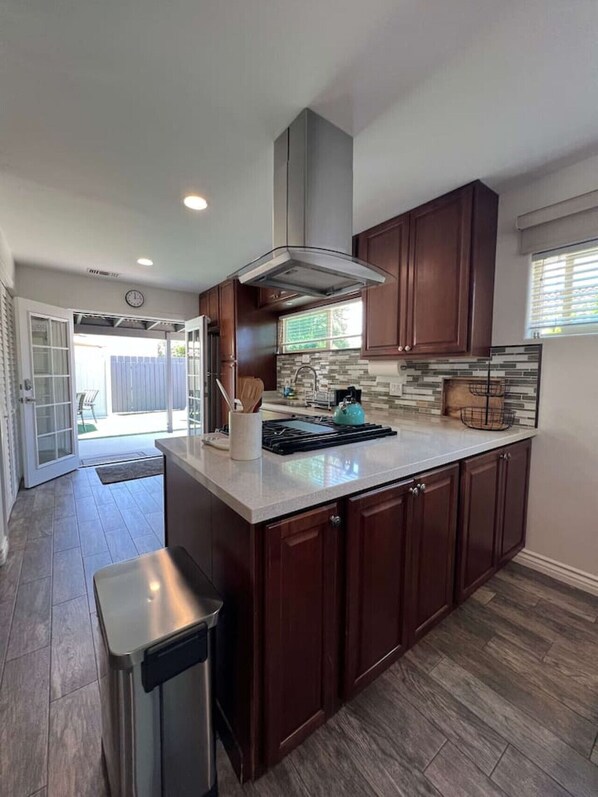 A modern kitchen with dark wood cabinets, a stainless steel range hood, and a large island with a sink.