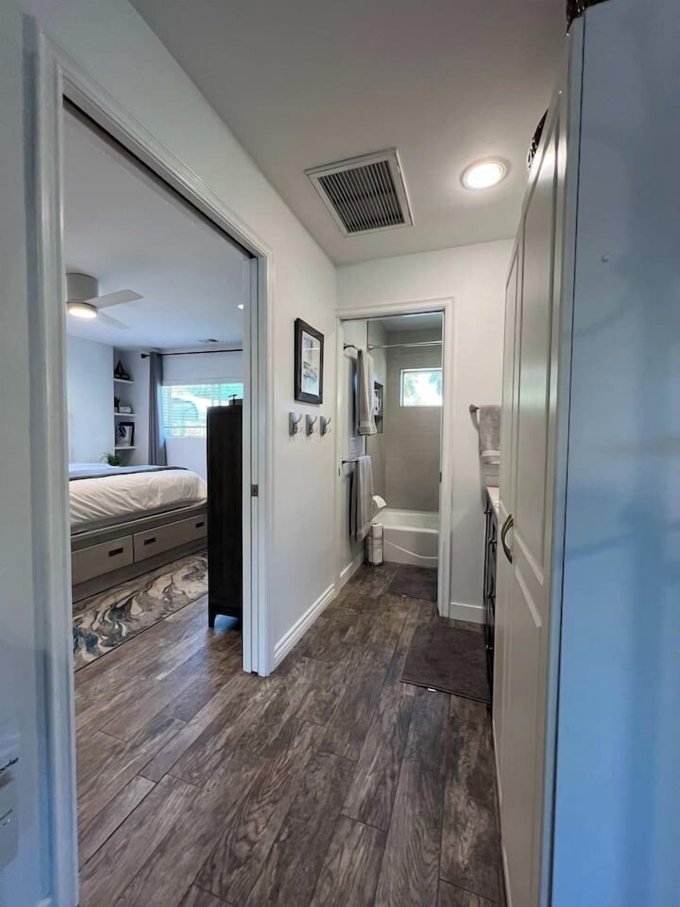 A hallway with a bed, a bathroom, and a refrigerator.