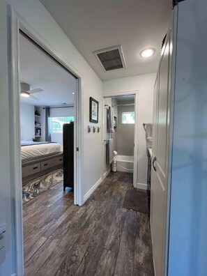 A hallway with a bed, a bathroom, and a refrigerator.