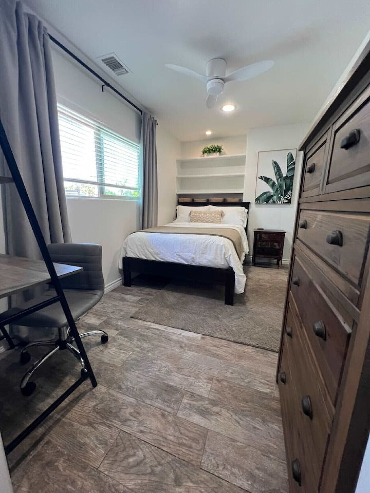 Un dormitorio con cama, escritorio, cómoda y ventilador de techo.