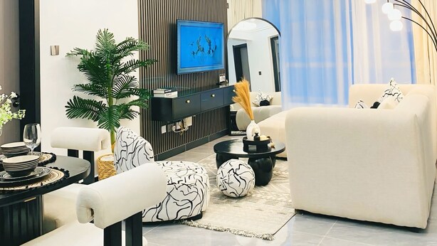 A modern living room with a flat-screen TV, a sofa, a dining table with chairs, and a large plant.