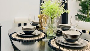A dining table with black and white plates, a vase with white flowers, and a black chair.