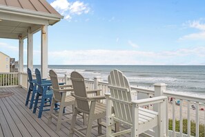A wooden deck with Adirondack chairs overlooking a beach.
