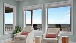 A room with two armchairs, a small round table, and a view of the ocean through large windows. - North Shore Paradise #199 - 7 BR, 7.5 BA Oceanfront Home w/ Pool & Hot Tub (Surf City)