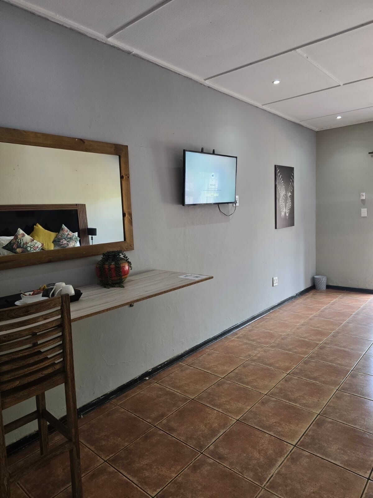 A room with a wooden chair, a small table with a decorative item, a flat-screen TV mounted on the wall, and a tiled floor.