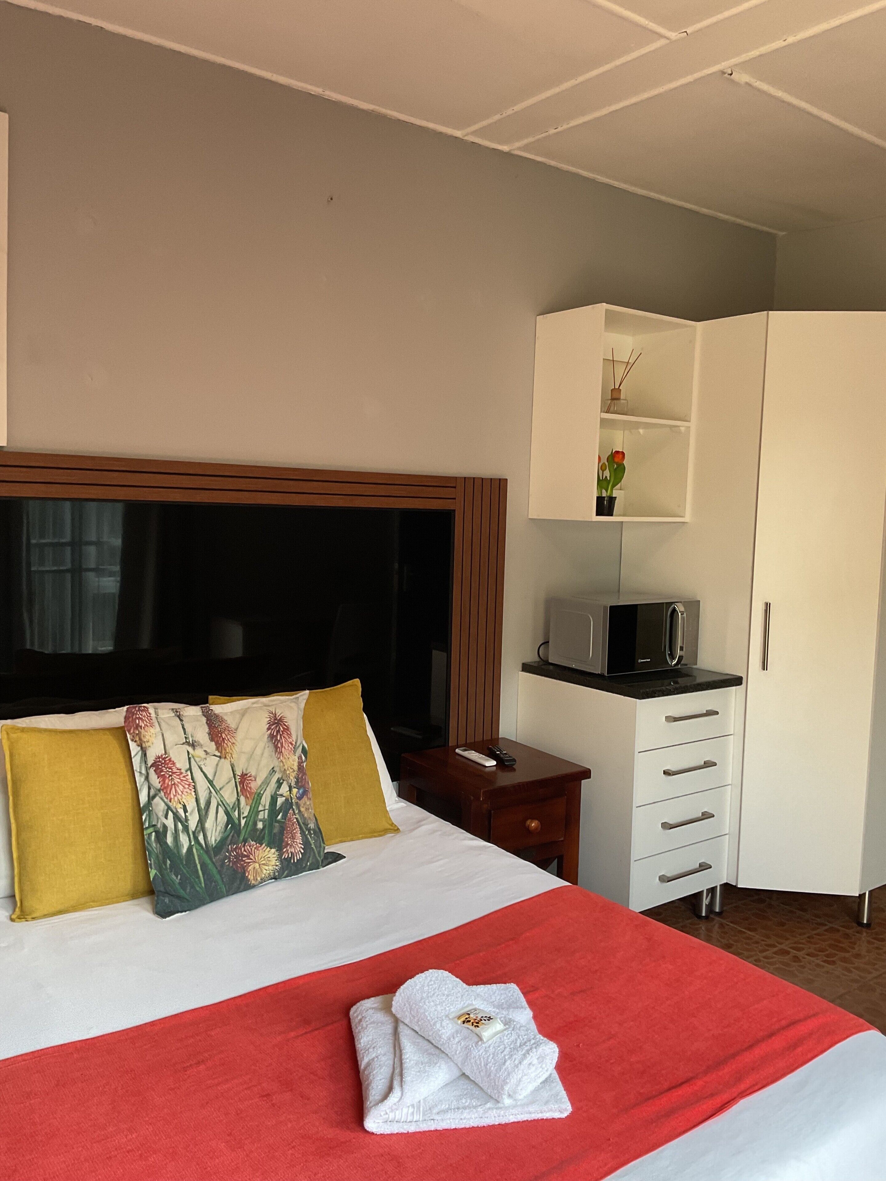 A hotel room with a bed, a TV, a microwave, a wardrobe, and a small table with a remote control.
