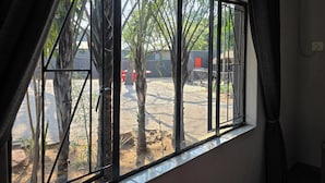A room with a large window overlooking a courtyard with palm trees and a red door. - Bothabelo Lodge (Phalaborwa)