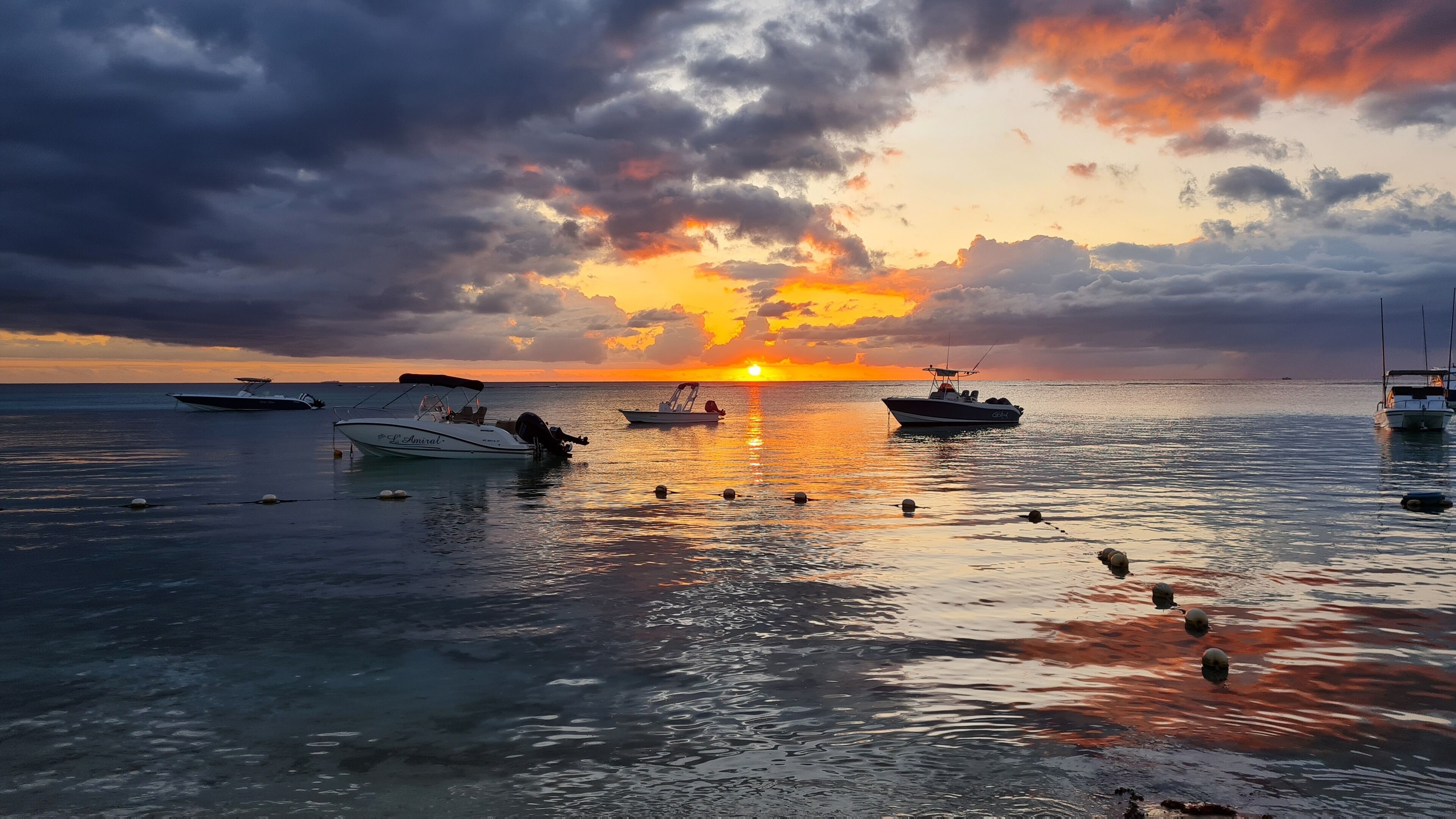 A sunset over a calm sea with boats anchored.